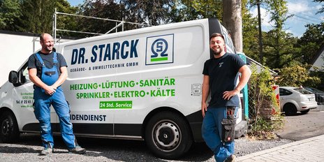 Zwei Handwerker stehen lächelnd vor einem Firmenwagen, der Dienstleistungen in Heizung, Sanitär und Elektro anbietet.